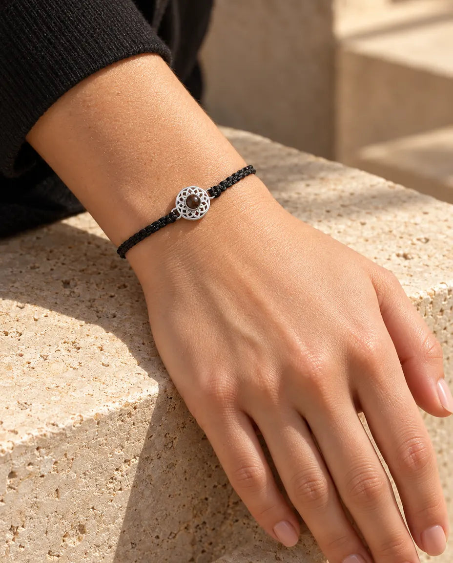 Femme portant le bracelet cordon fin tressé noir avec médaillon rond argenté au poignet, sous une lumière chaude