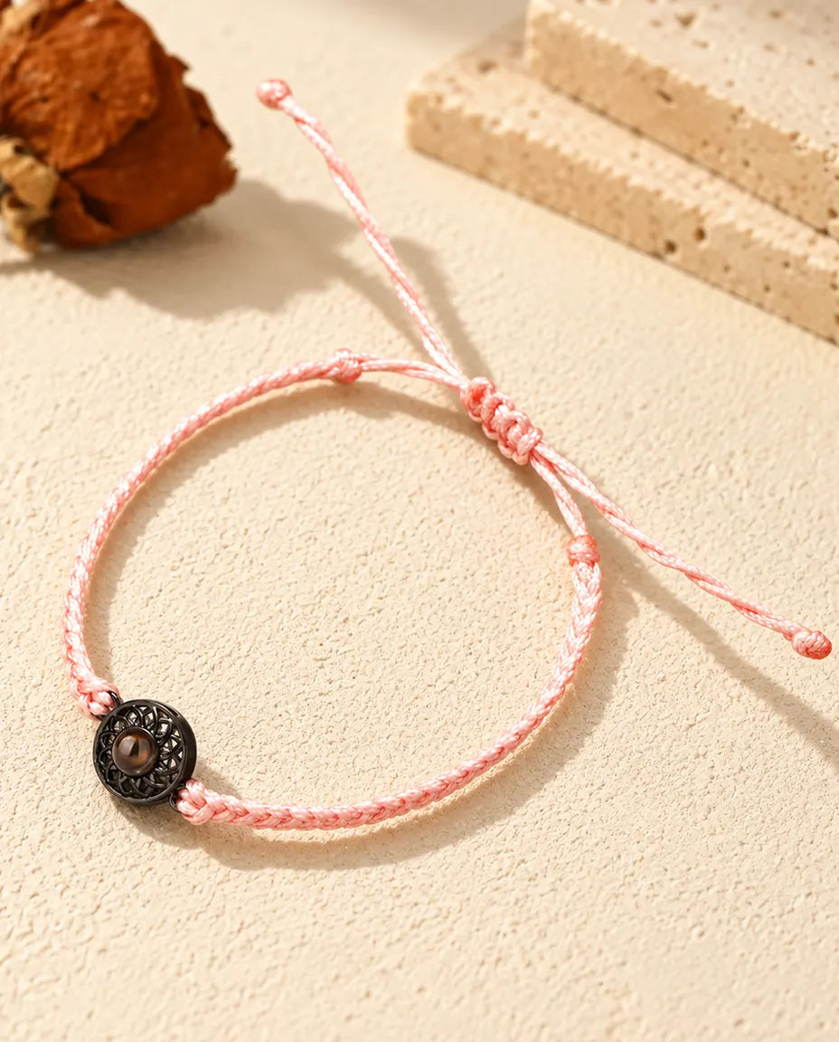Bracelet cordon fin tressé rose avec médaillon rond noir et pierre de projection brune sur plâtre