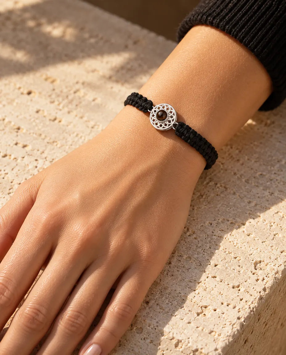 Femme portant le bracelet cordon tressé noir avec médaillon rond argenté au poignet, sous une lumière chaude