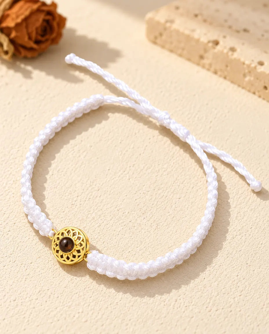 Bracelet cordon tressé blanc avec médaillon rond doré et nœud coulissant sur plâtre clair