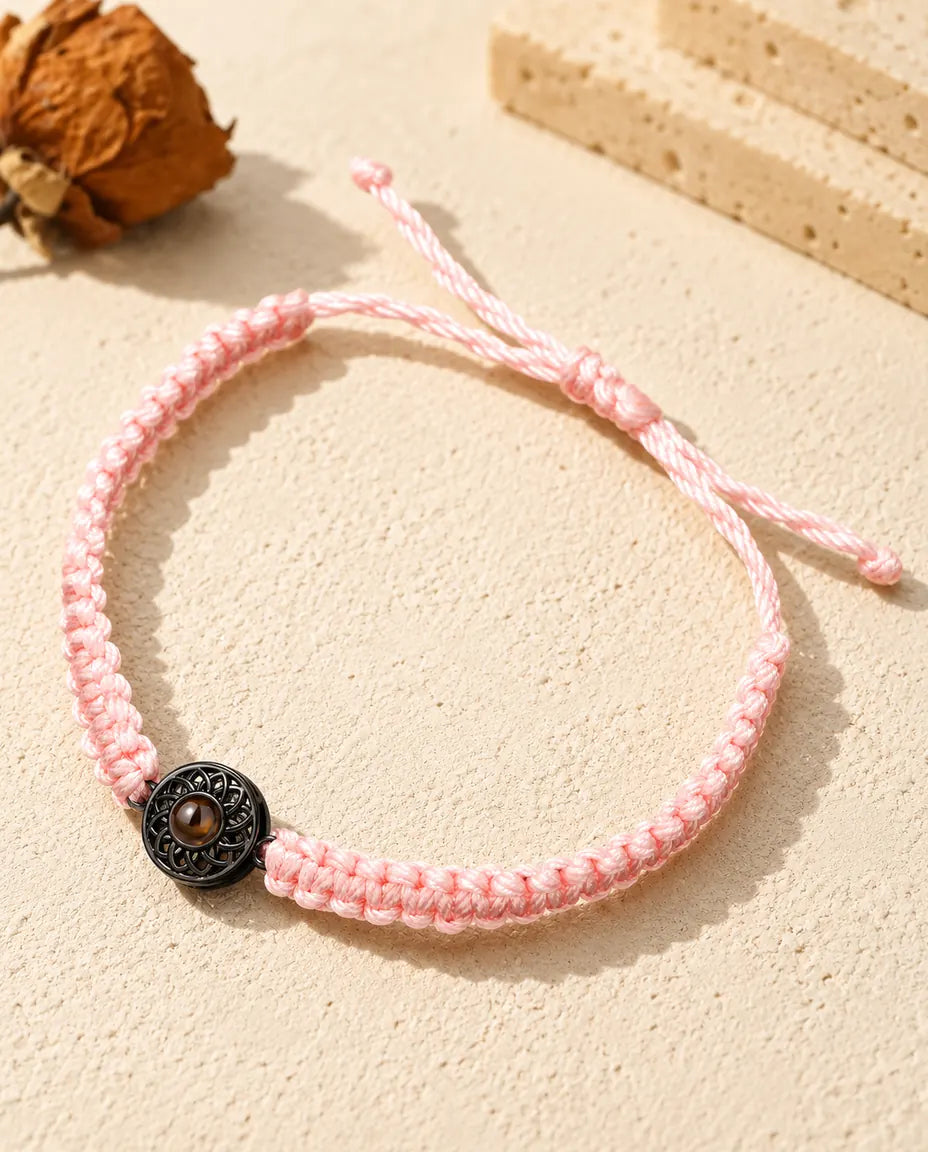 Bracelet cordon tressé rose avec médaillon rond noir et pierre de projection brune sur plâtre