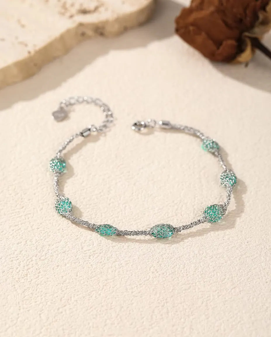 Bracelet Zircons en Cage en Argent 925 - version zircons verts près d’une dalle de travertin et d’une rose séchée