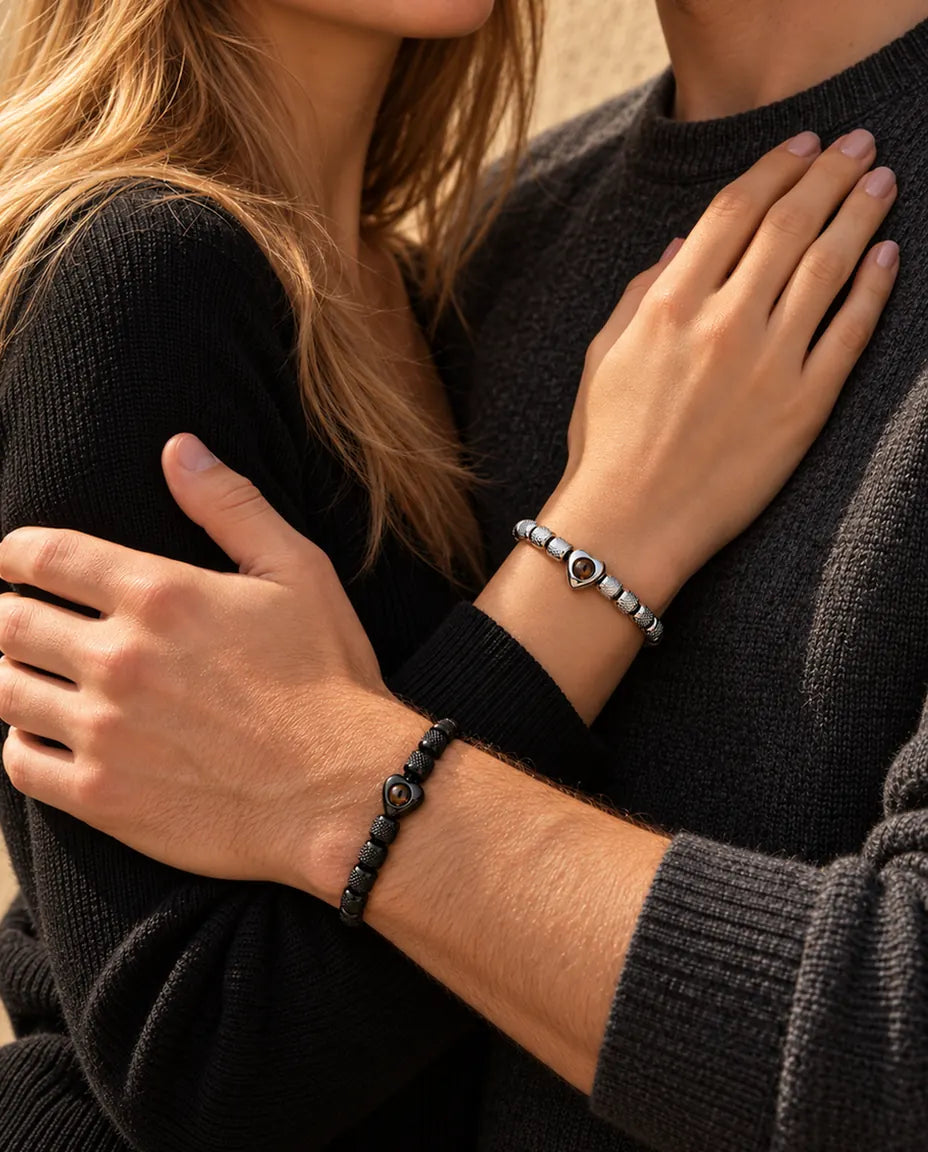 Couple enlacé : elle porte le bracelet argenté à perle cœur, lui le bracelet noir