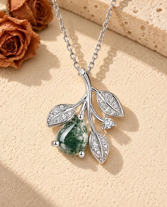 Collier Agate Mousse Feuilles en Argent 925 - posé sur une surface claire texturée près d’un bloc de travertin