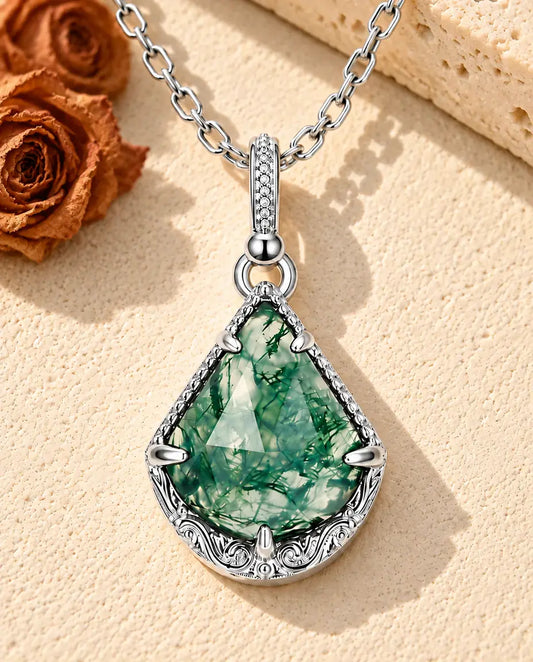 Collier Agate Mousse Écusson en Argent 925 - posé sur une surface claire texturée près d’un bloc de travertin
