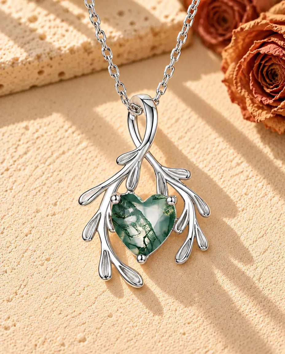 Collier Agate Mousse Cœur et Branches en Argent 925 - posé sur une surface claire texturée près d’un bloc de travertin