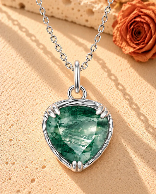 Collier Pendentif Cœur Agate Mousse en Argent 925 - posé sur une surface claire texturée près d’un bloc de travertin
