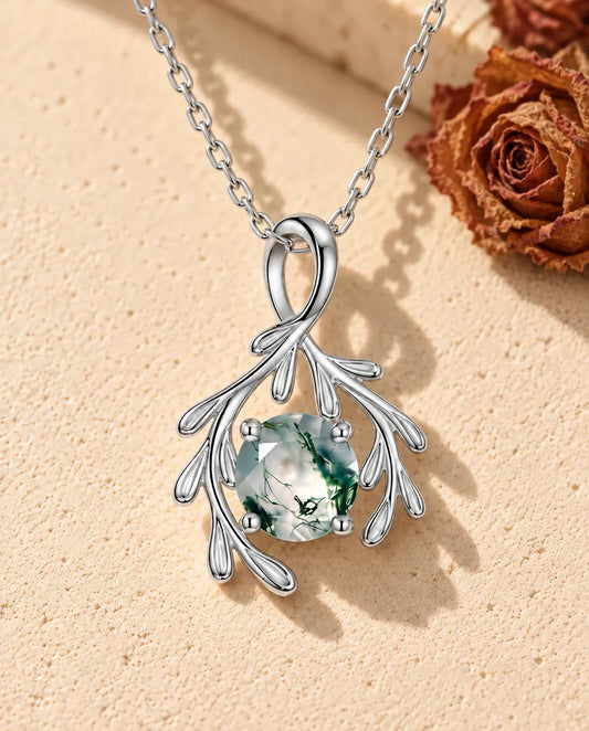 Collier Agate Mousse Branche en Argent 925 - posé sur une surface claire texturée près d’un bloc de travertin