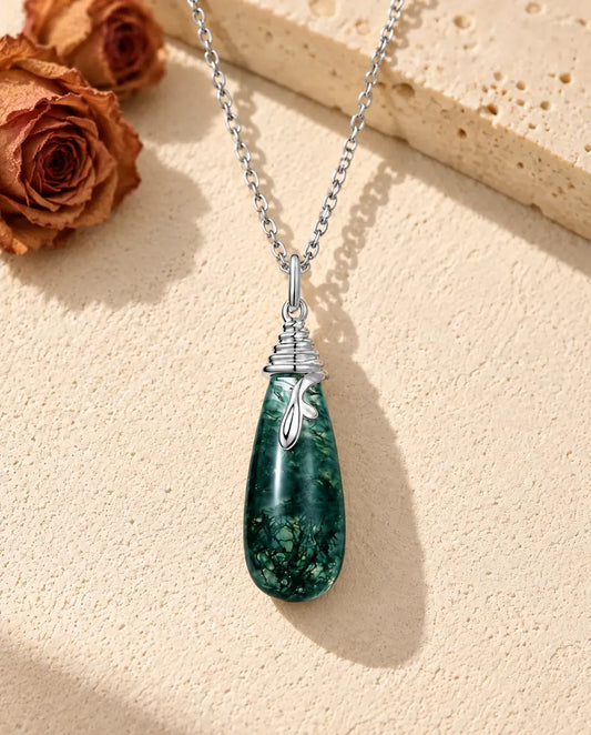 Collier Agate Mousse Goutte en Argent 925 - posé sur une surface claire texturée près d’un bloc de travertin