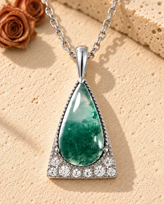 Collier Agate Mousse Triangle en Argent 925 - posé sur une surface claire texturée près d’un bloc de travertin