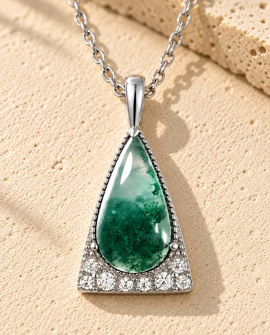 Collier Agate Mousse Triangle en Argent 925 - posé sur une surface claire texturée près d’un bloc de travertin