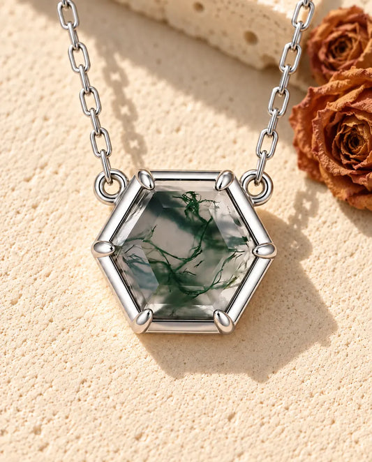Collier Agate Mousse Hexagonale en Argent 925 - posé sur une surface claire texturée près d’un bloc de travertin
