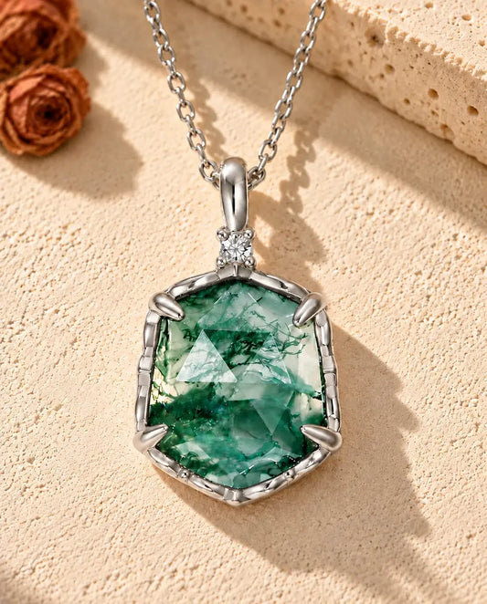 Collier Agate Mousse Hexagonale en Argent 925 - posé sur une surface claire texturée près d’un bloc de travertin