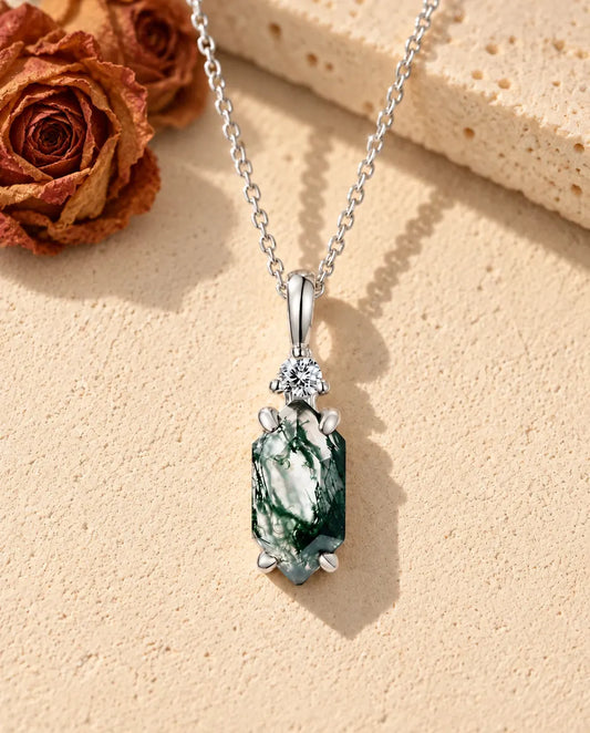 Collier Agate Mousse Hexagone Fin en Argent 925 - posé sur une surface claire texturée près d’un bloc de travertin
