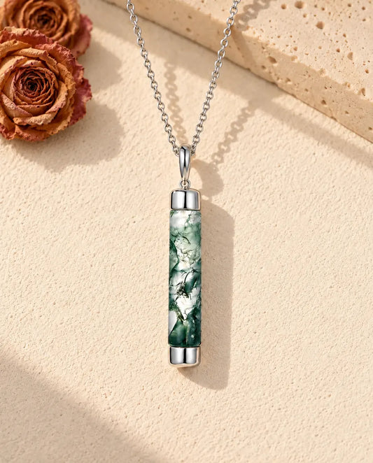 Collier Agate Mousse Long Cylindre en Argent 925 - posé sur une surface claire texturée près d’un bloc de travertin