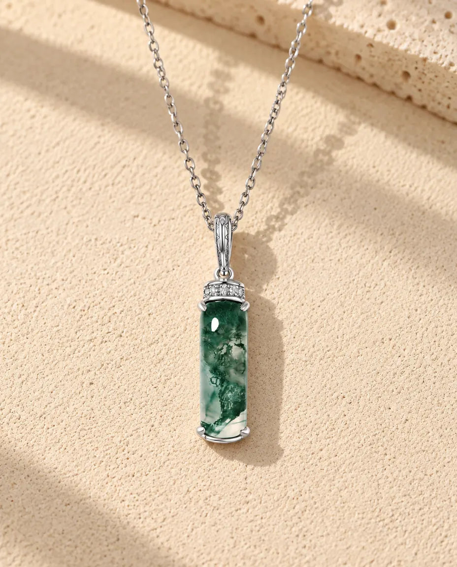 Collier Agate Mousse Longue Barrette en Argent 925 - posé sur une surface claire texturée près d’un bloc de travertin