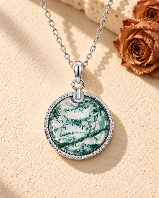 Collier Agate Mousse Médaillon Rond en Argent 925 - posé sur une surface claire texturée près d’un bloc de travertin