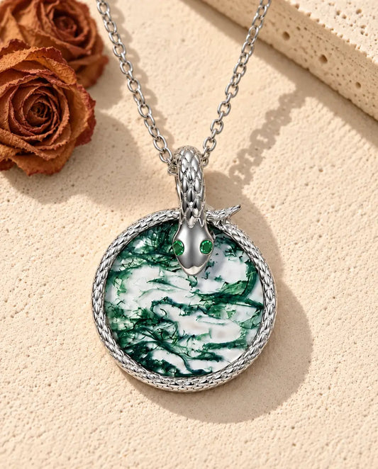 Collier Agate Mousse Serpent en Argent 925 - posé sur une surface claire texturée près d’un bloc de travertin