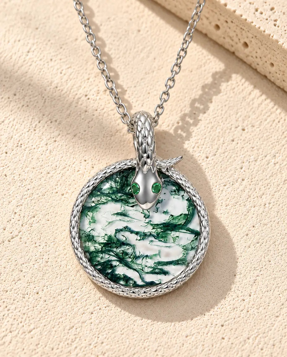 Collier Agate Mousse Serpent en Argent 925 - posé sur une surface claire texturée près d’un bloc de travertin