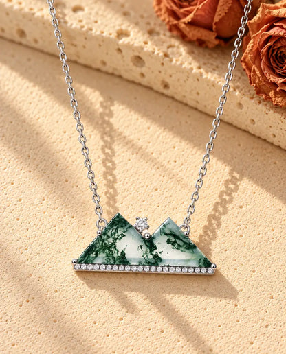 Collier Montagne Agate Mousse en Argent 925 - posé sur une surface claire texturée près d’un bloc de travertin
