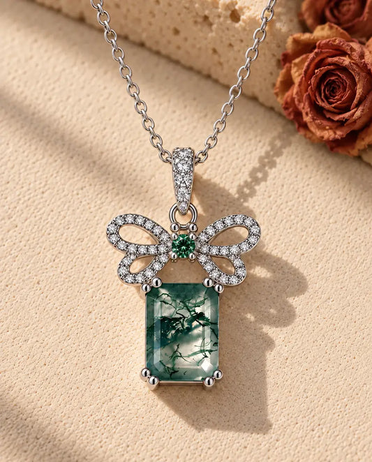 Collier Agate Mousse Nœud en Argent 925 - posé sur une surface claire texturée près d’un bloc de travertin