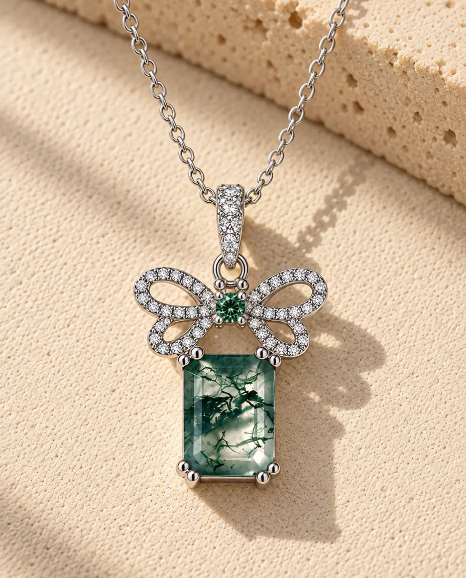 Collier Agate Mousse Nœud en Argent 925 - posé sur une surface claire texturée près d’un bloc de travertin