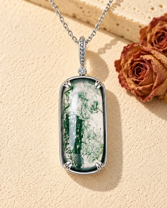 Collier Agate Mousse Pendentif Rectangle en Argent 925 - posé sur une surface claire texturée près d’un bloc de travertin