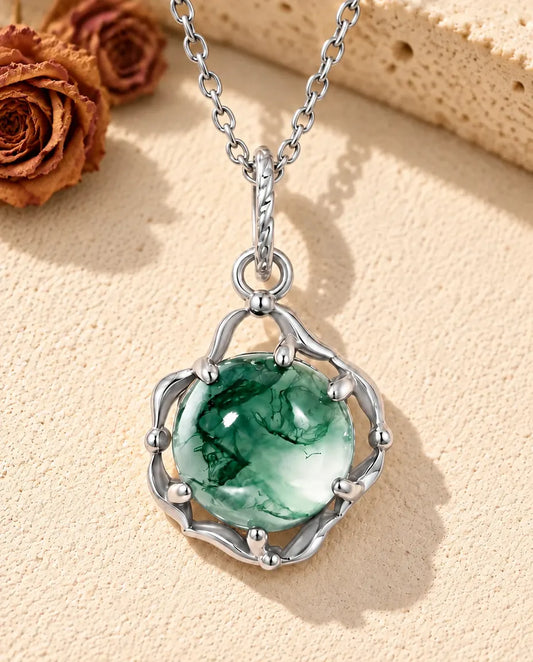 Collier Agate Mousse Ronde en Argent 925 - posé sur une surface claire texturée près d’un bloc de travertin