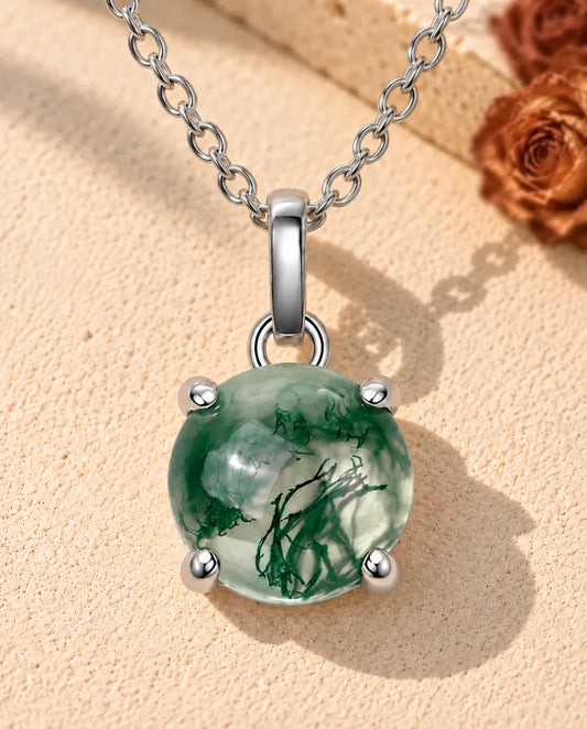 Collier Agate Mousse Ronde en Argent 925 - posé sur une surface claire texturée près d’un bloc de travertin