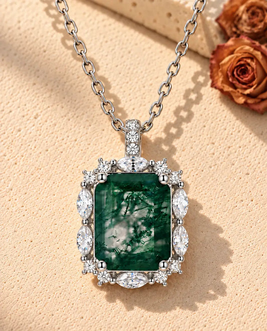 Collier Agate Mousse Taille Émeraude en Argent 925 - posé sur une surface claire texturée près d’un bloc de travertin