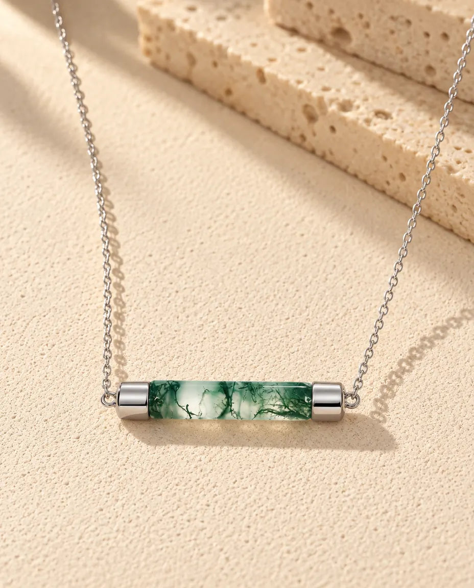 Collier Barre Agate Mousse en Argent 925 - posé sur une surface claire texturée près d’un bloc de travertin