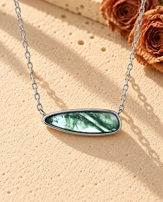 Collier Barrette Agate Mousse en Argent 925 - posé sur une surface claire texturée près d’un bloc de travertin