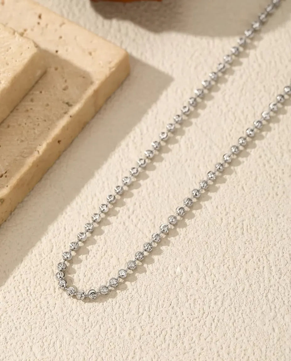 Collier Perles Facettées en Argent 925 - posé sur une surface claire près d’une dalle de travertin