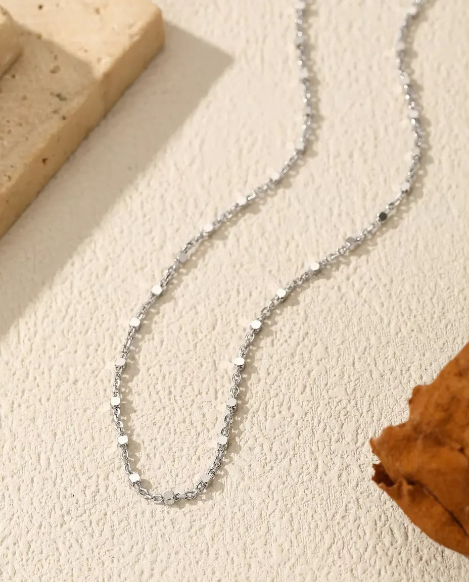 Collier Chaîne à Paillettes en Argent 925 - posé sur une surface claire près d’une dalle de travertin