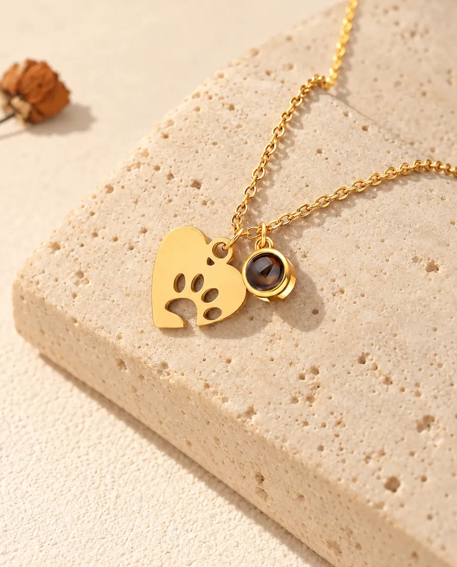 Collier cœur patte doré avec petite pierre de projection posé sur du travertin