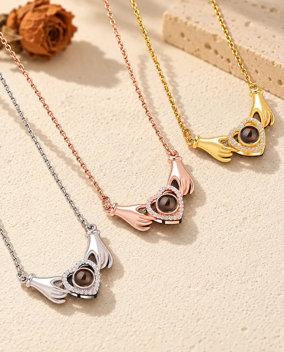 Le collier mains et cœur en argenté, couleur or rose et doré, posés côte à côte sur du plâtre