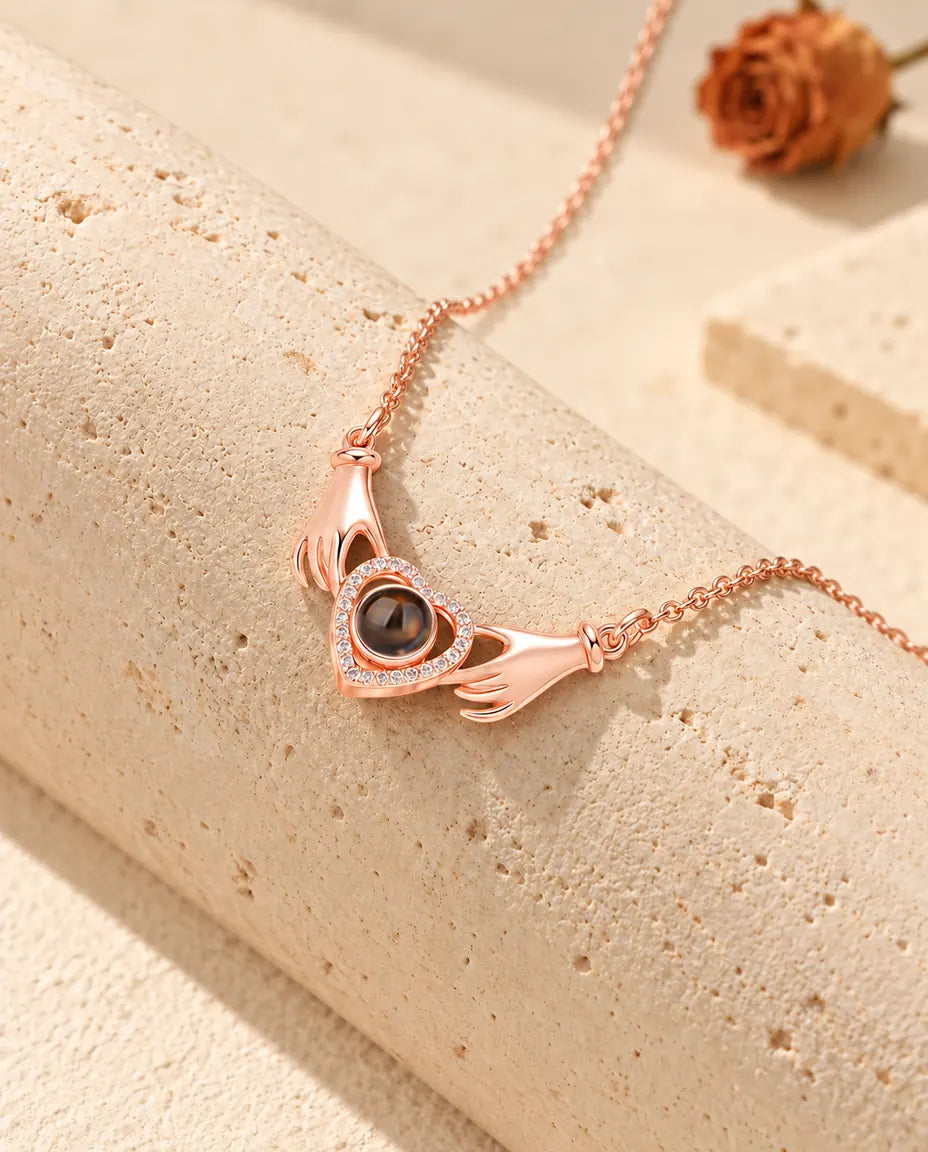 Collier photo projection couleur or rose aux mains tenant un cœur, drapé sur un bloc de travertin