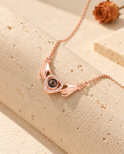 Collier photo projection couleur or rose aux mains tenant un cœur, drapé sur un bloc de travertin