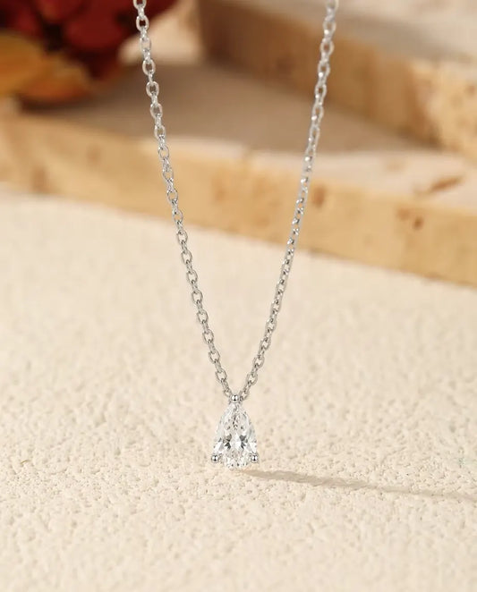 Collier Moissanite Poire 1 ct en Argent 925 - pendentif posé sur une surface claire près d’une dalle de travertin