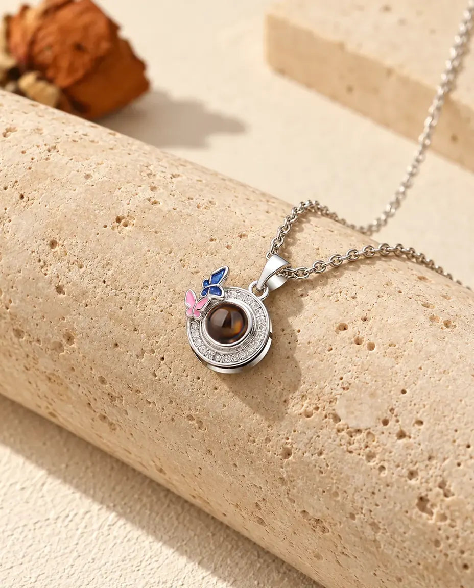 Collier photo projection personnalisé argenté avec papillons émaillés bleu nuit et rose sur du travertin