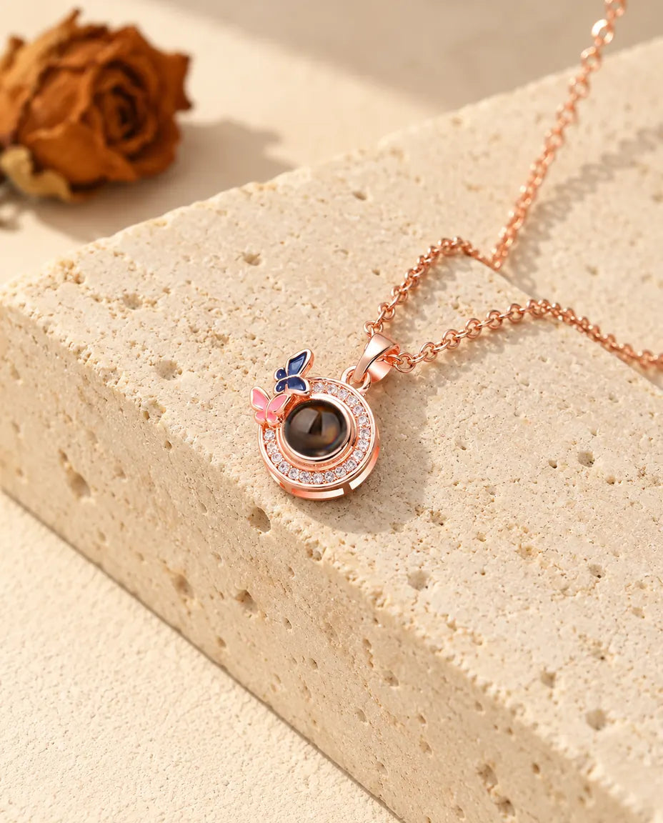 Médaille couleur or rose cerclée de zircons avec deux papillons émaillés contre du travertin