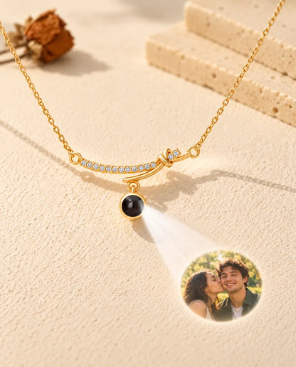 Collier barre courbée doré projetant une photo de couple sur le plâtre crème