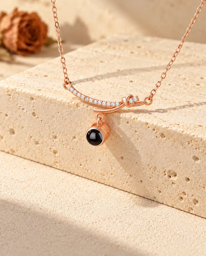 Collier barre courbée couleur or rose avec sa pierre de projection pendante sur du travertin