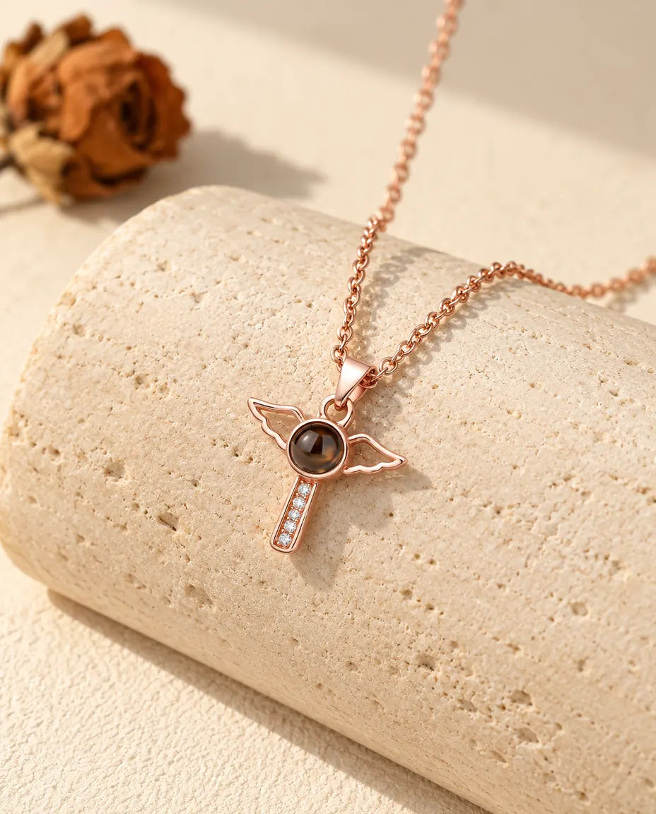 Collier croix aux ailes d'ange couleur or rose posé sur un bloc de travertin