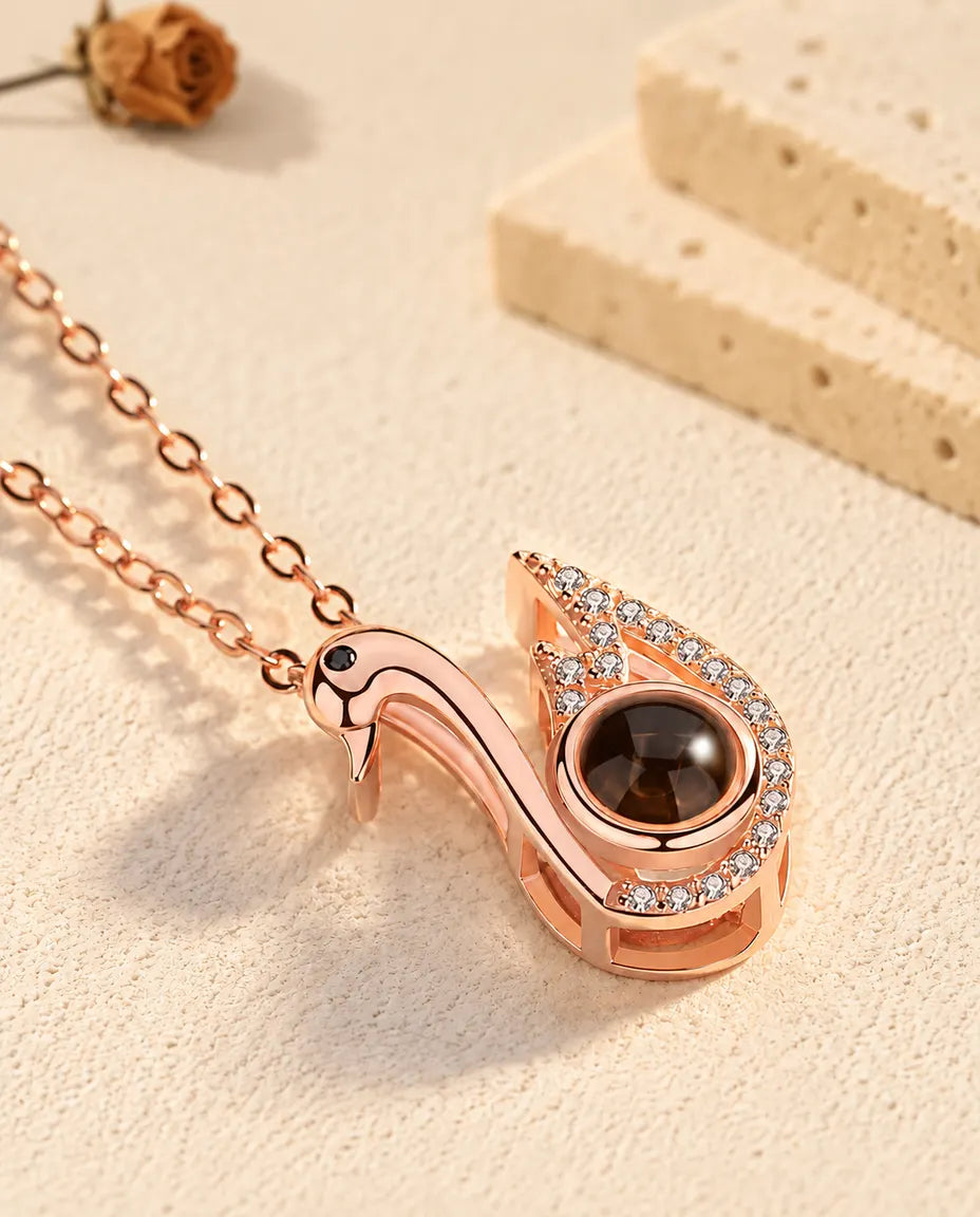 Pendentif cygne couleur or rose incliné sur le plâtre crème