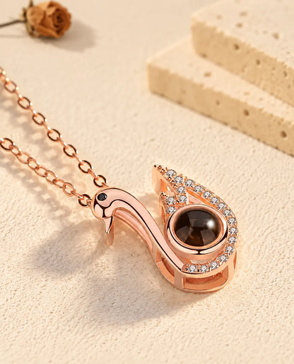 Pendentif cygne couleur or rose incliné sur le plâtre crème