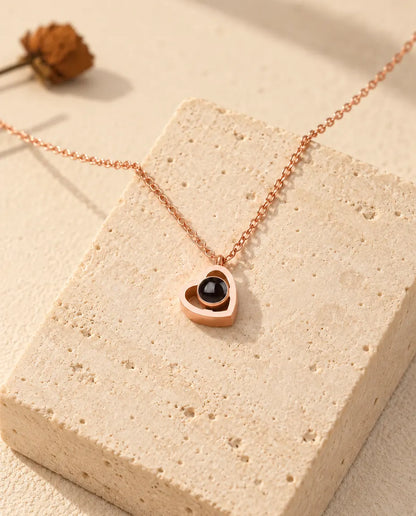 Collier photo projection double cœur couleur or rose posé sur un bloc de travertin