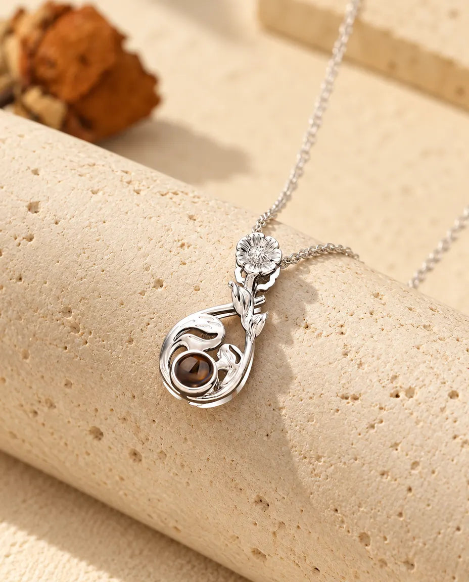 Collier goutte à marguerite argenté posé sur un bloc de travertin