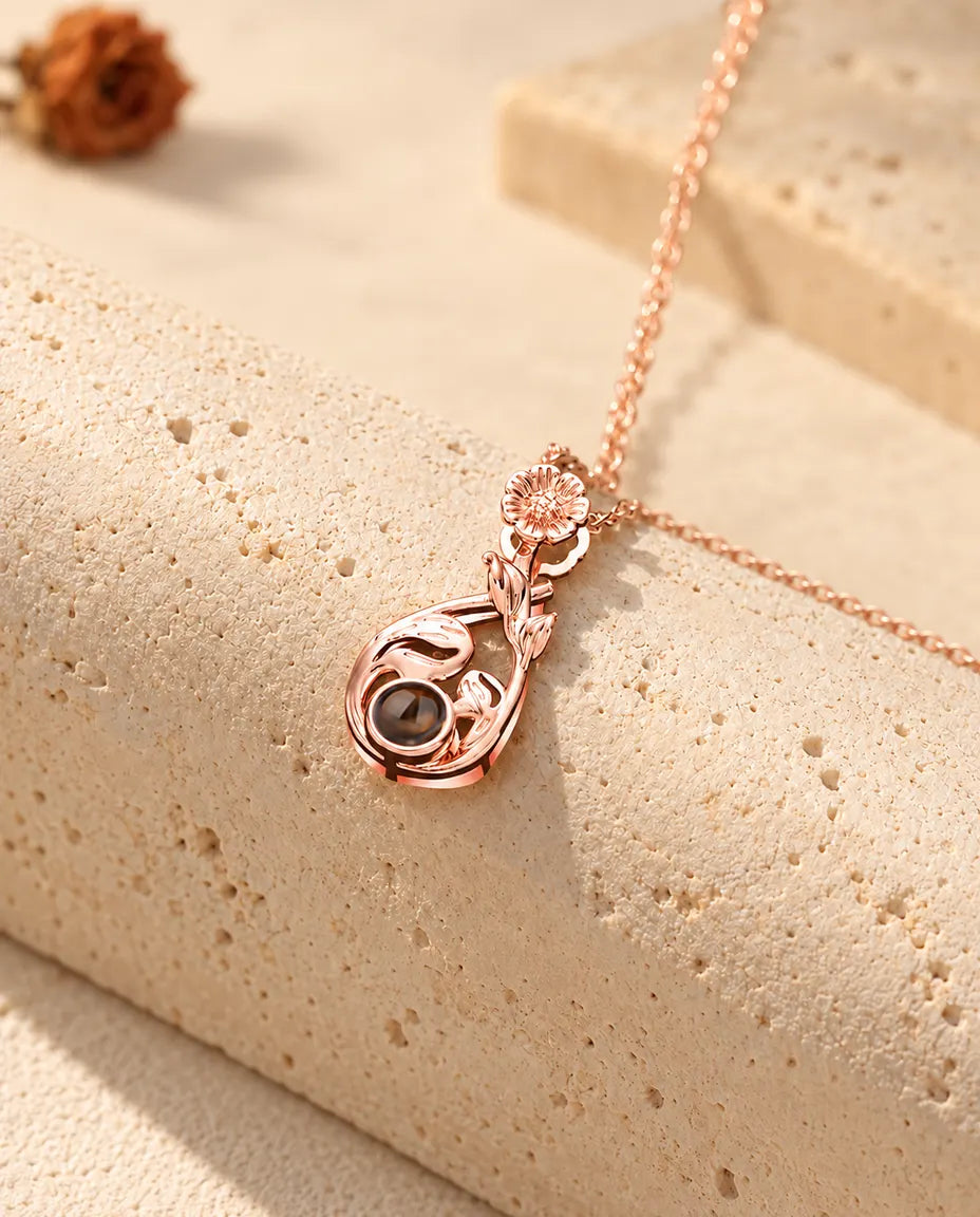 Collier goutte à marguerite couleur or rose posé sur un bloc de travertin