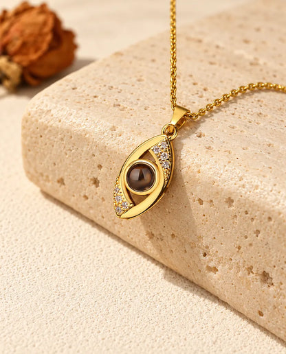Collier mauvais œil doré avec photo dans la pierre posé sur un bloc de travertin